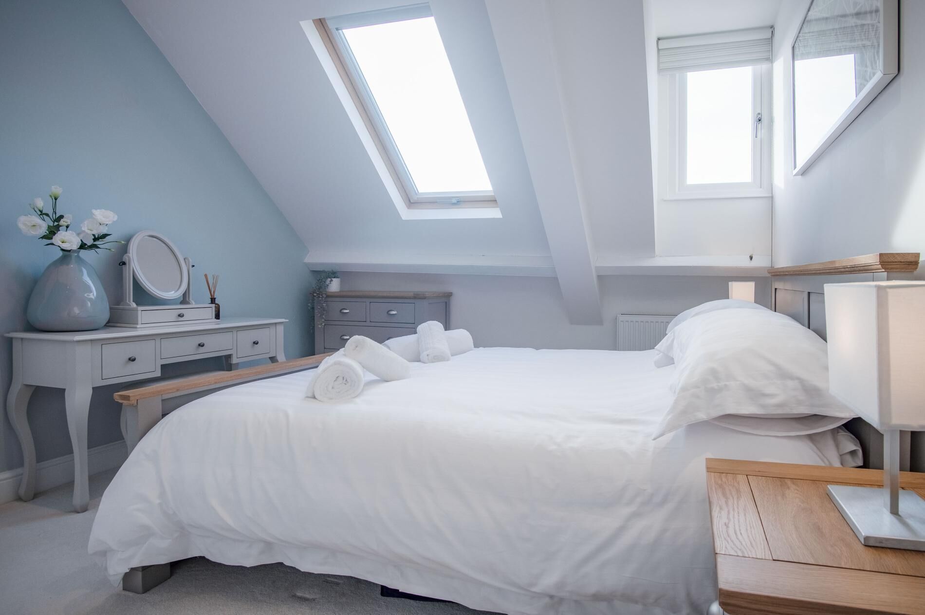 Un dormitorio con tragaluz, una cama, un tocador con espejo y una mesita de noche.