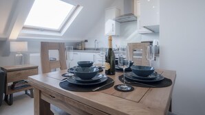 A modern kitchen with a skylight, a dining table set with dinnerware, and a bottle of champagne. - Skylark - 2 Bedroom Apartment - Tenby (Tenby)