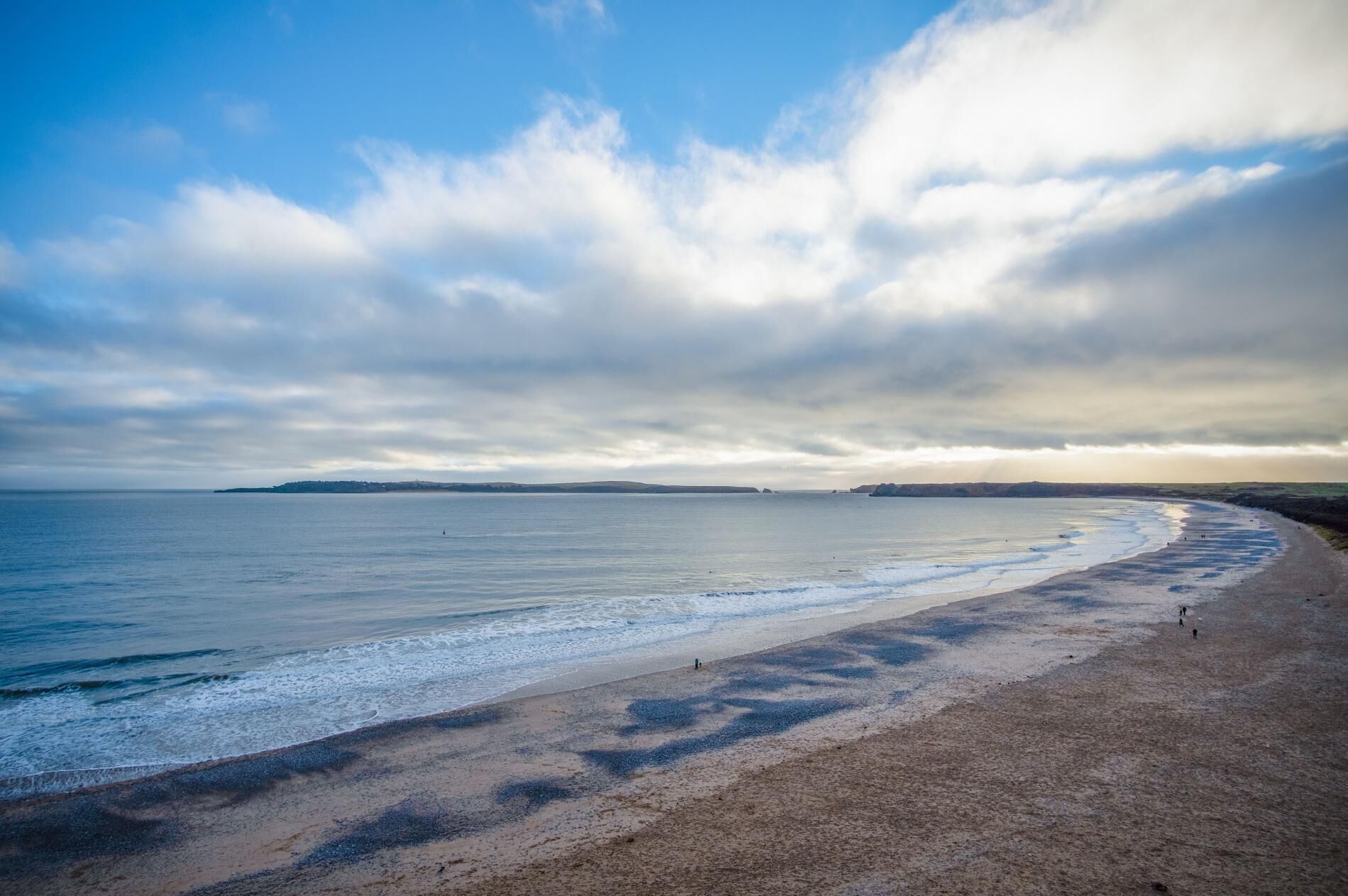 Une plage avec un large rivage sablonneux et une mer calme sous un ciel partiellement nuageux.