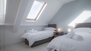 A modern bedroom with two beds, a skylight, and a small bedside table with a lamp. - Skylark - 2 Bedroom Apartment - Tenby (Tenby)
