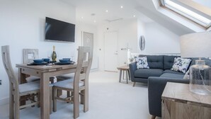 A modern living space with a dining area, a sofa, and a TV mounted on the wall. - Skylark - 2 Bedroom Apartment - Tenby (Tenby)