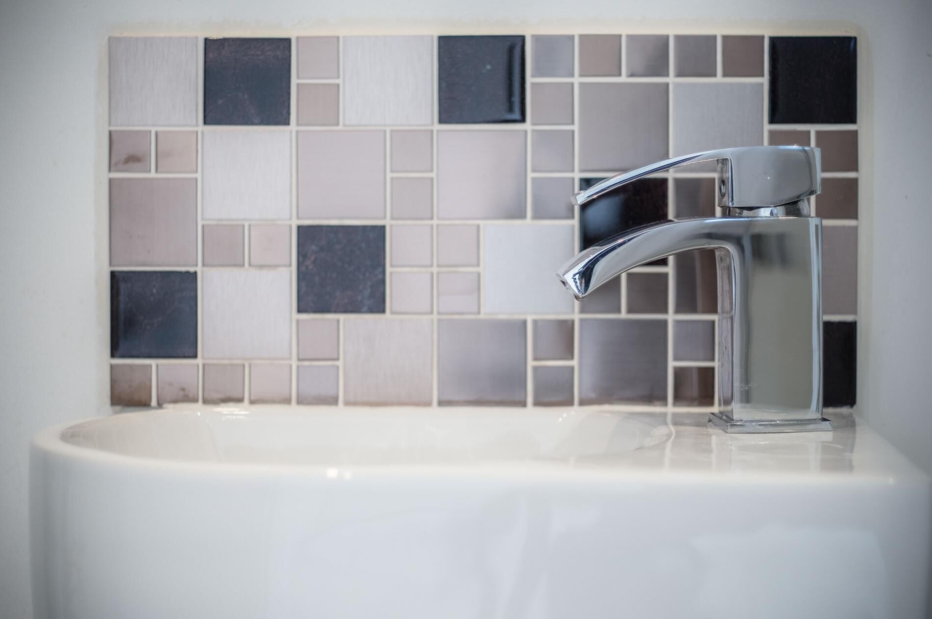 A bathroom with a white sink, chrome faucet, and a tiled backsplash.