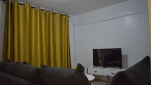 A living room with a sofa, a television on a white cabinet, and yellow curtains. - Cozy stay in Langata (Nairobi)