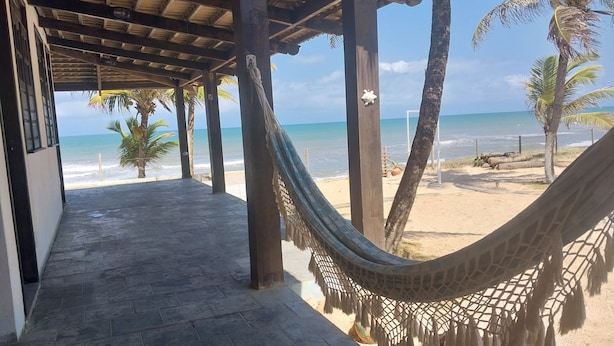 A covered walkway with a hammock, palm trees, and a beach view. - Pousada Marinheiro (Conde)