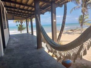 A covered walkway with a hammock, palm trees, and a beach view.