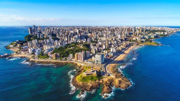 An aerial view of a coastal city with high-rise buildings, a lighthouse, and a beach.