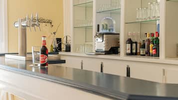 Zona de bar con grifo de cerveza, dispensador de refrescos y una vitrina que contiene botellas y vasos.