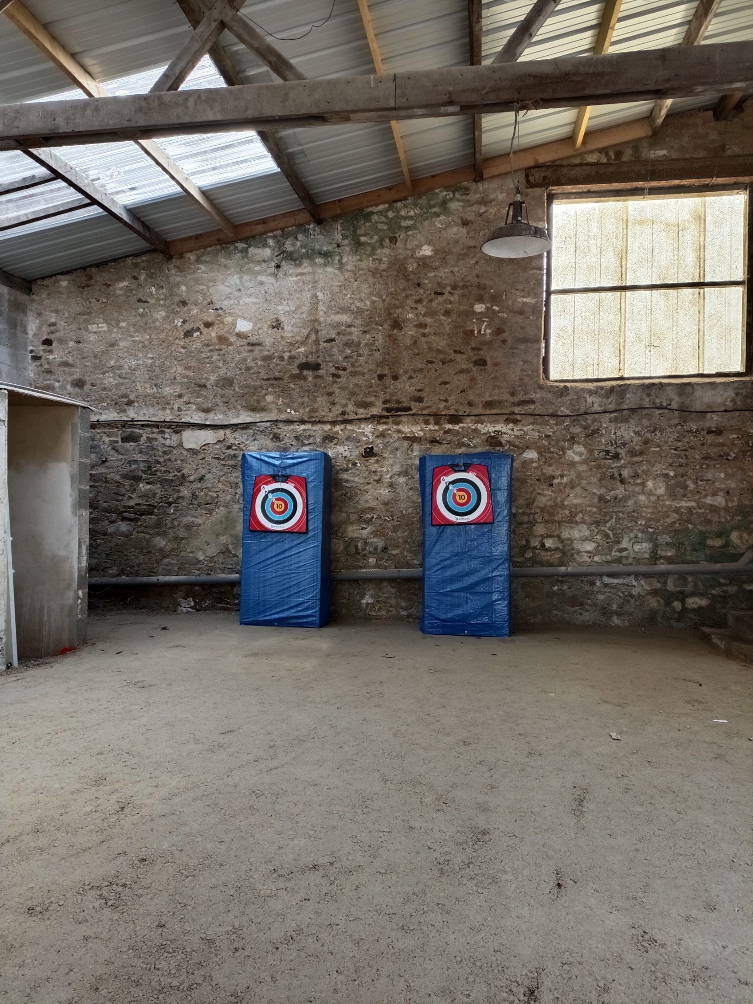 A rustic room with a high ceiling, stone walls, and two blue target boards.