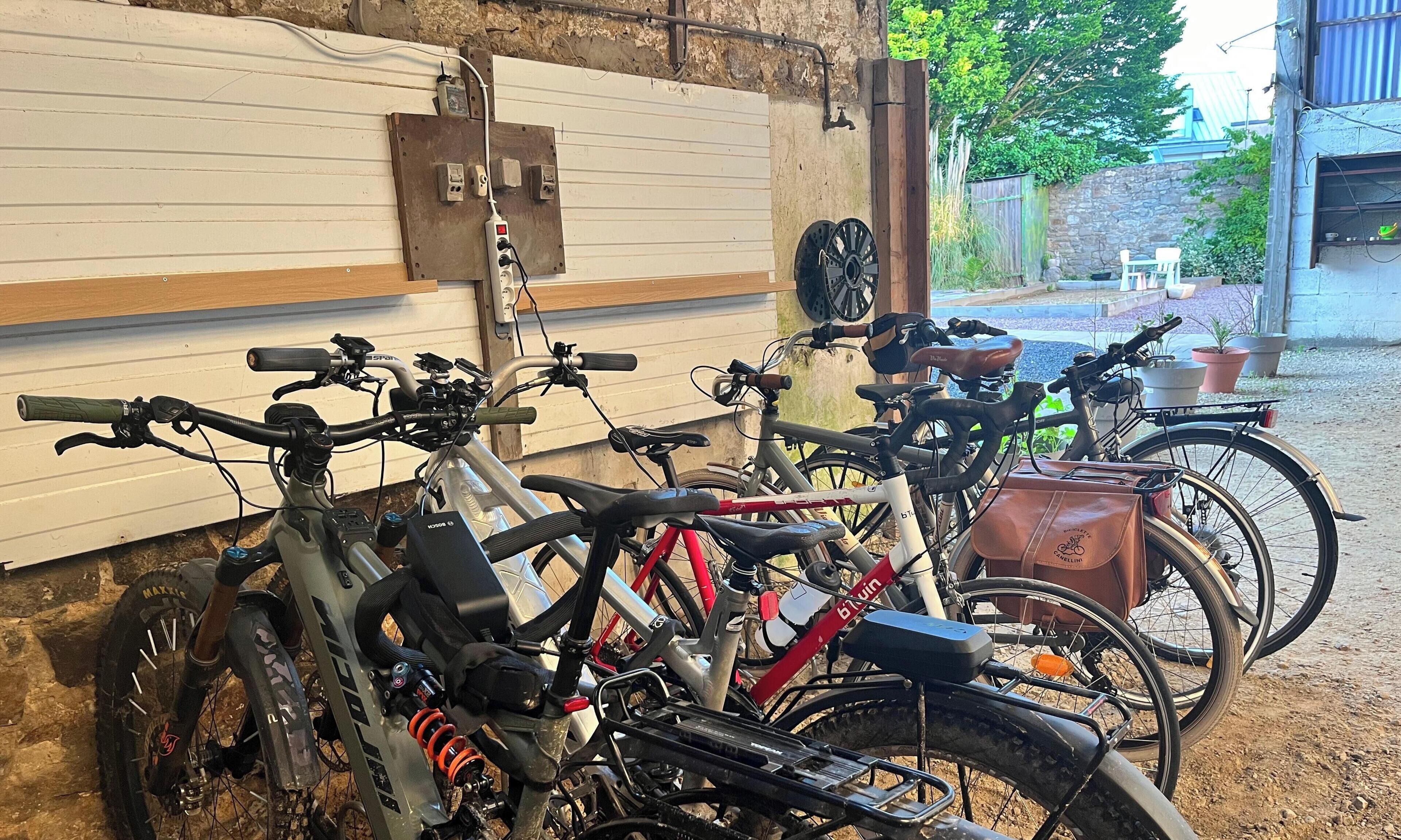 Bicycles parked indoors with a wall-mounted electrical outlet and a window with a view of the outside.
