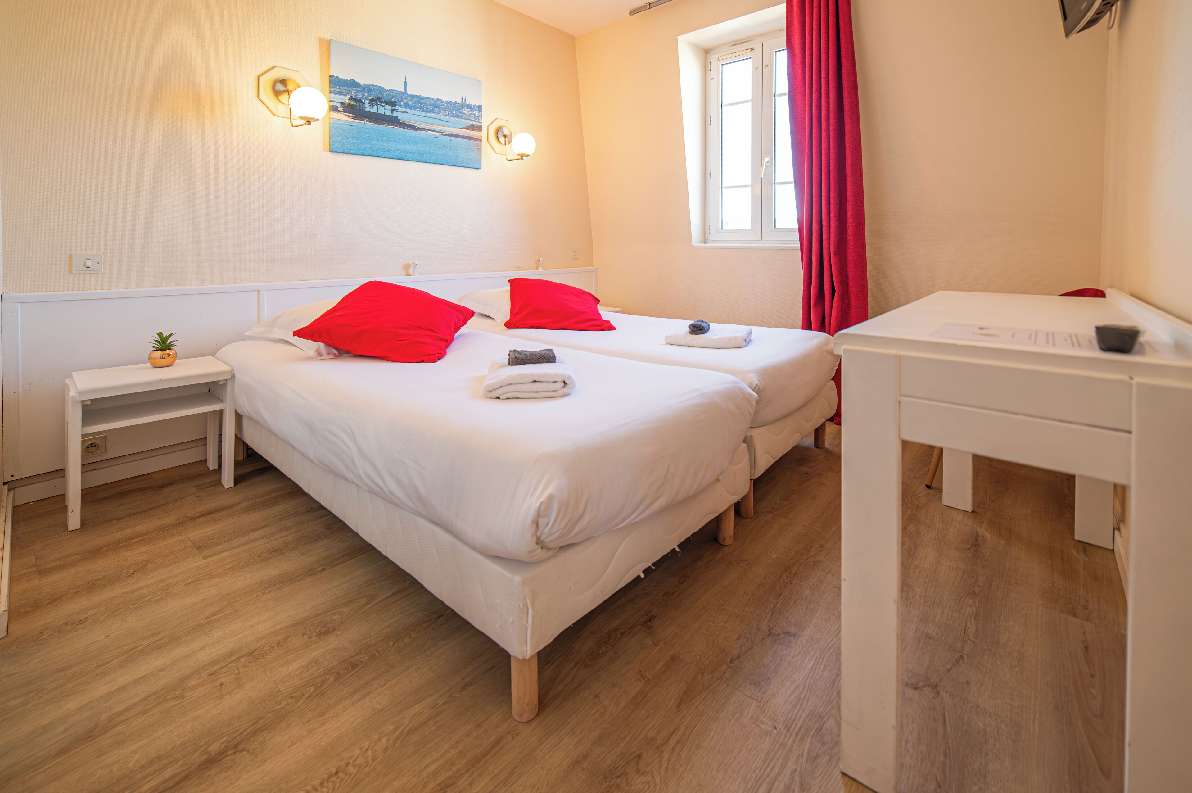 Une chambre d’hôtel avec deux lits, un bureau, une petite table et une fenêtre avec des rideaux rouges.