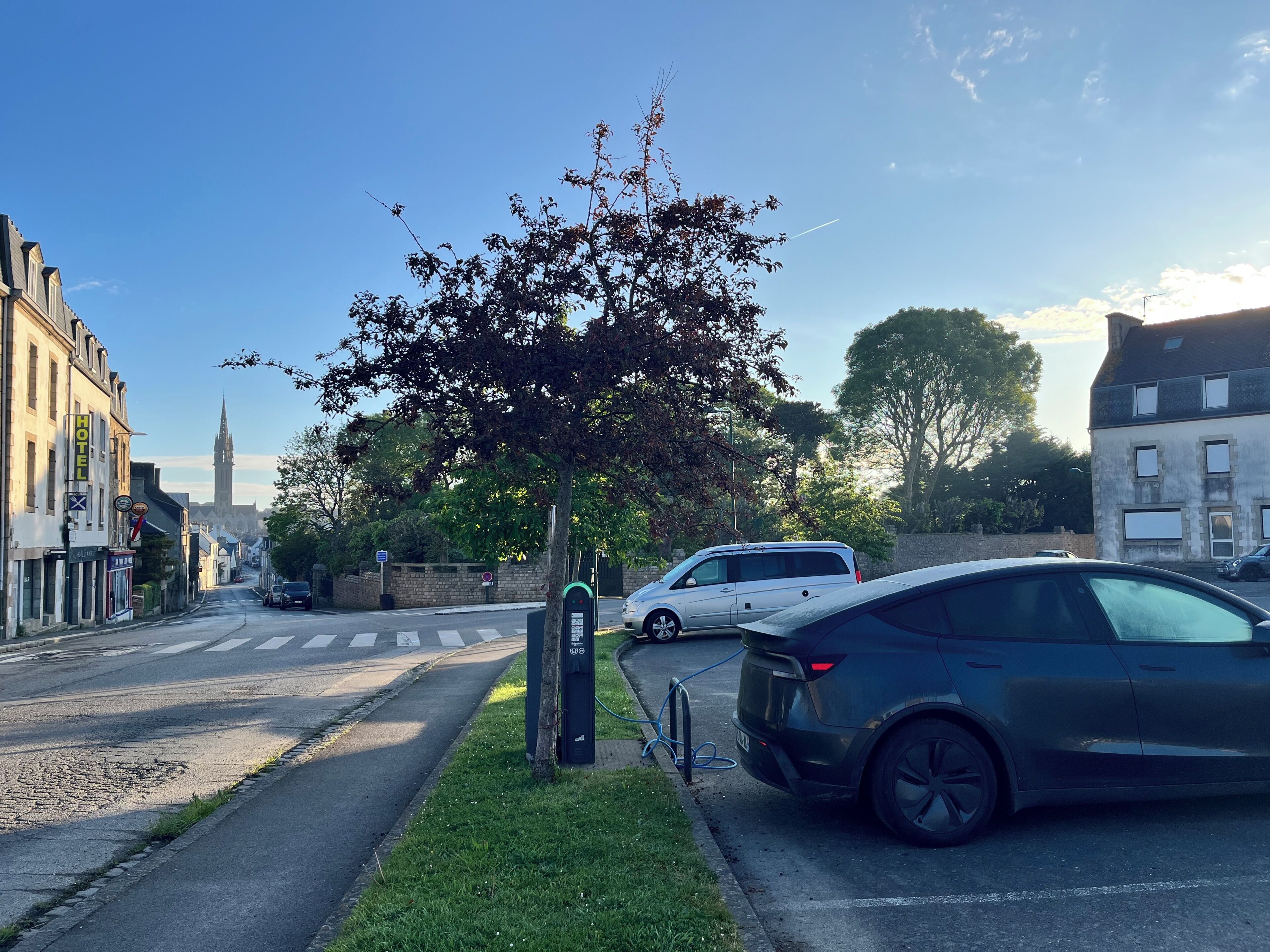 A street with parked cars, a tree, and buildings including a hotel.
