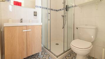A bathroom with a glass-enclosed shower, a toilet, and a wooden vanity with a mirror.