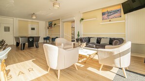 Een moderne woonkamer met een pooltafel, comfortabele zitplaatsen en een flatscreen televisie aan de muur.