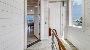 Um corredor com painéis brancos, teto de madeira e vista para uma sala de jantar com mesa e cadeiras.