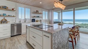 Uma cozinha moderna com armários brancos, uma ilha central e vista para o oceano.