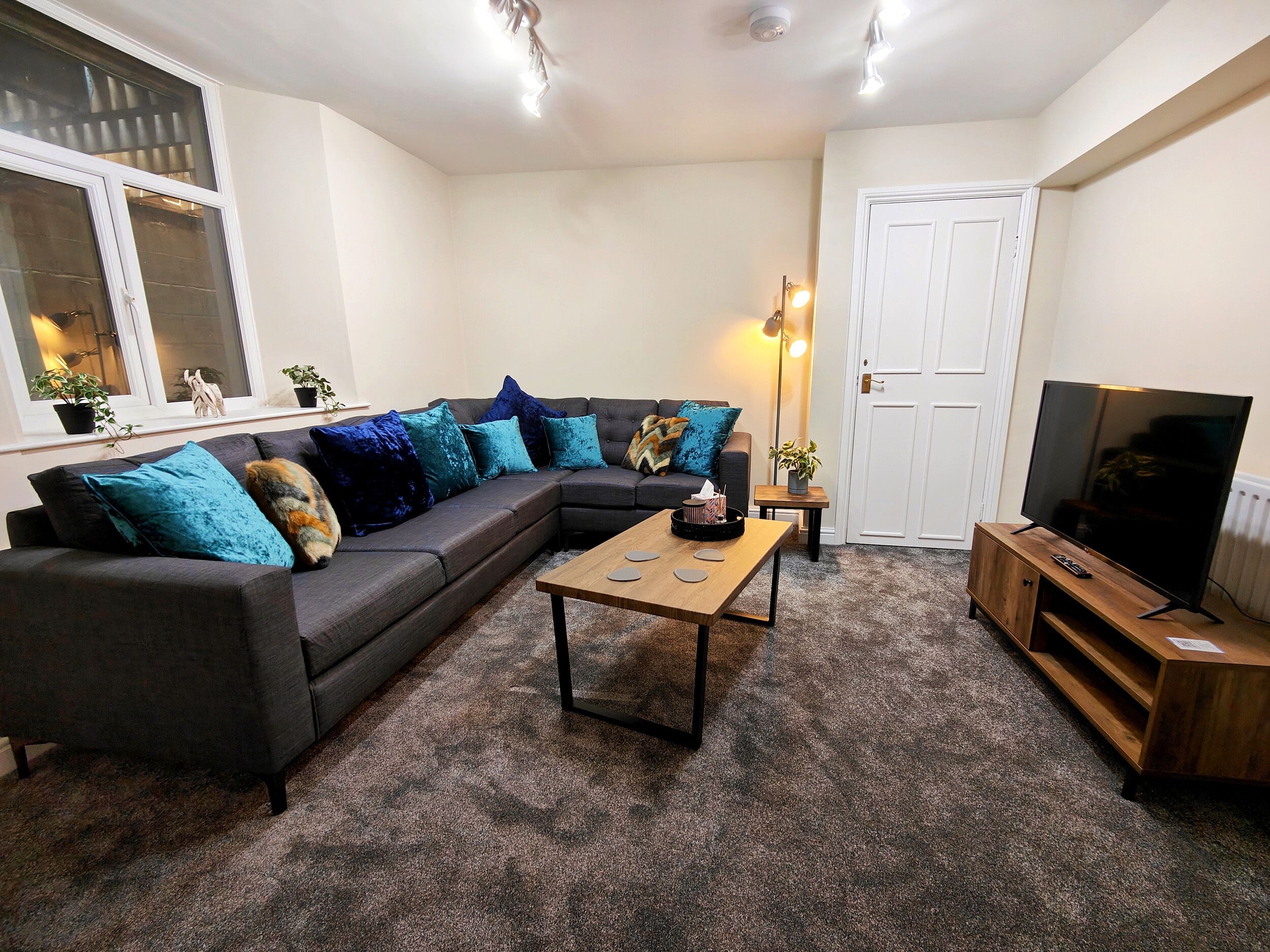 A living room with a sectional sofa, a coffee table, a TV on a wooden stand, and a door.