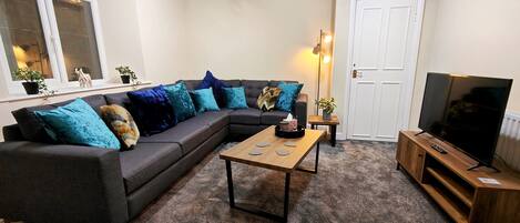 A living room with a sectional sofa, a coffee table, a TV on a wooden stand, and a door.