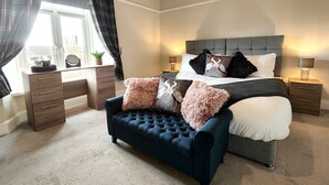 Une chambre à coucher avec un canapé capitonné, un lit avec de nombreux coussins, un bureau et une fenêtre avec des rideaux.