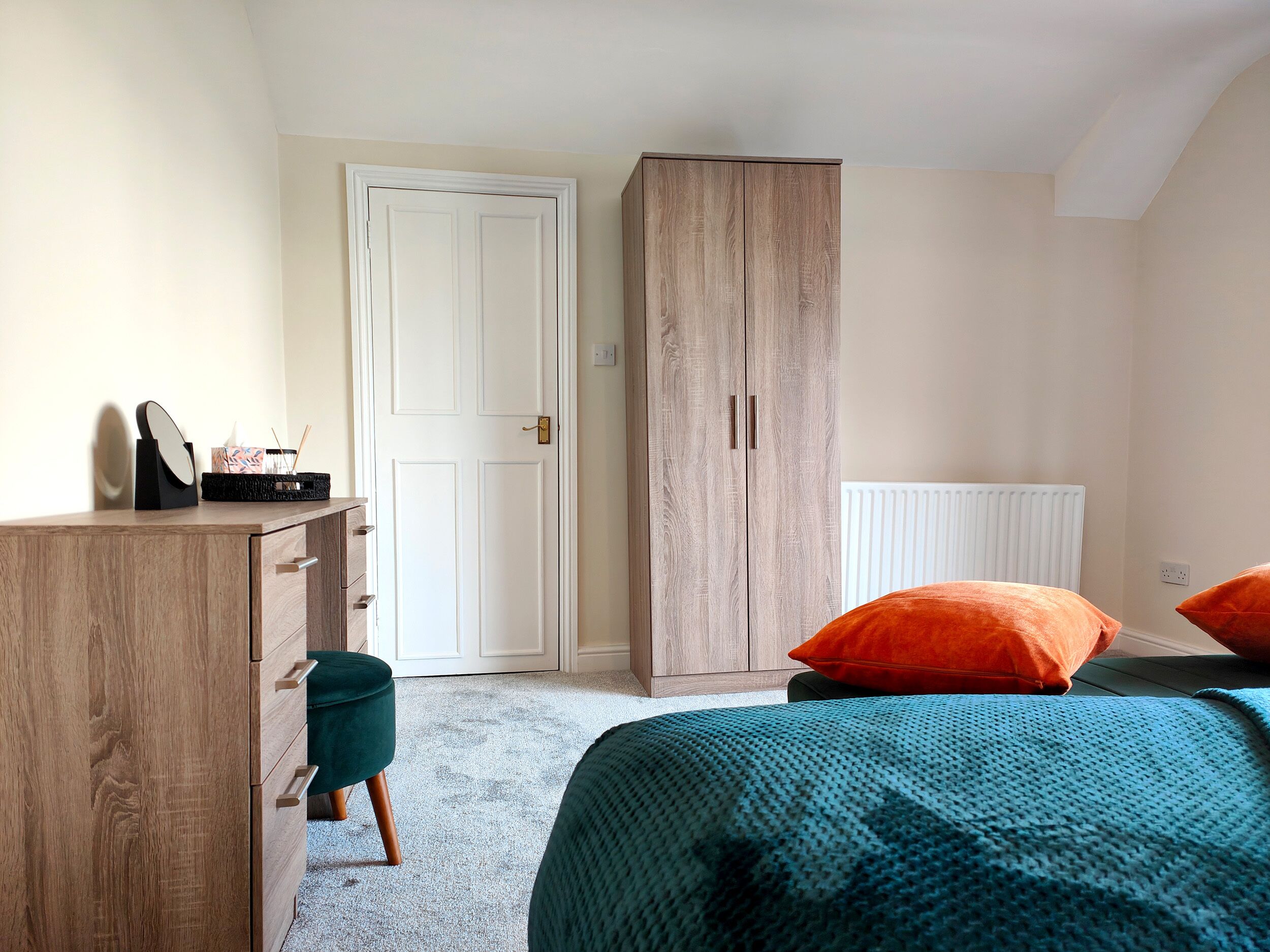 A bedroom with a wooden desk, a wardrobe, and a bed with orange pillows.