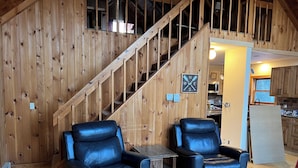 Un intérieur en bois avec un escalier, deux fauteuils en cuir, une petite table et un coin cuisine.