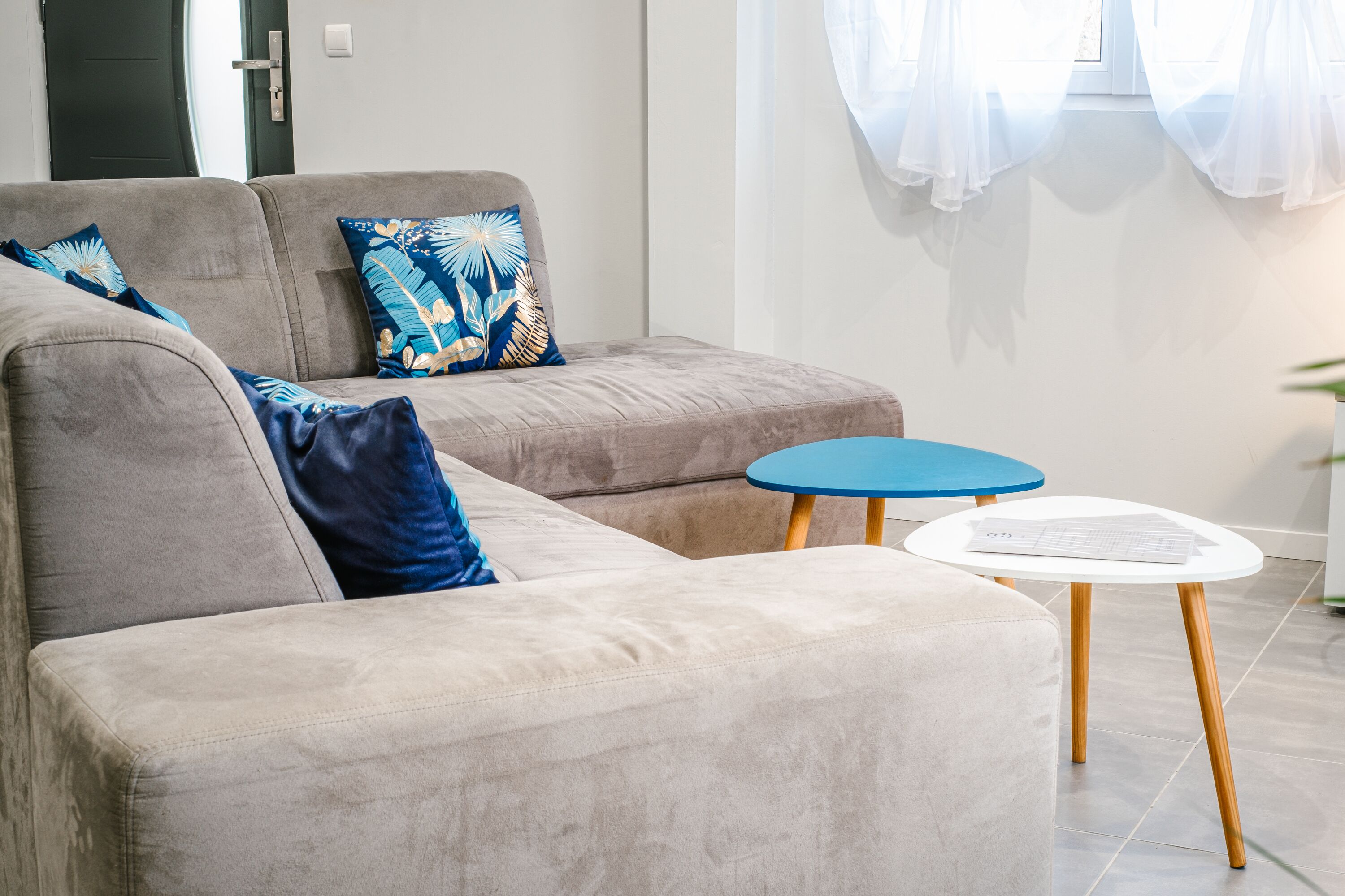 A modern living room with a grey sofa, blue cushions, and a small white table with wooden legs.