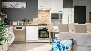 Eine moderne Küche mit weißen Schränken, einer eingebauten Mikrowelle und einem Herd. Es gibt einen Essbereich mit einem grauen Sofa und einem blau gemusterten Kissen.