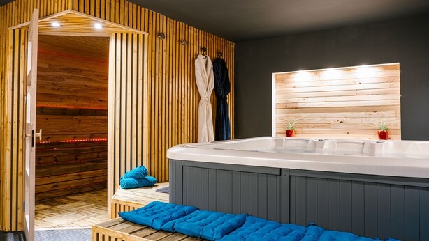 Ein moderner Spa-Bereich mit Wandverkleidung aus Holzlamellen, einer Whirlwanne und blau gepolsterten Sitzgelegenheiten.