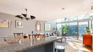A modern kitchen with a granite countertop, a hanging light fixture, and a view of the backyard through large windows.