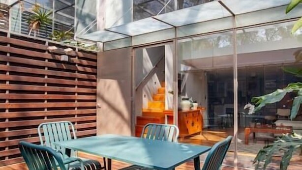 A modern outdoor patio with a glass-enclosed dining area, wooden deck, and a view of the surrounding trees.