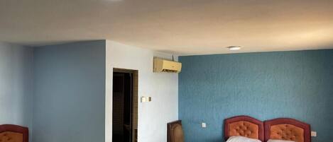 A room with two beds, a chair, and an air conditioning unit.