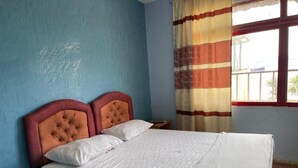 Un lit doté d’une tête de lit capitonnée, de draps blancs et d’une fenêtre ornée de rideaux à rayures.