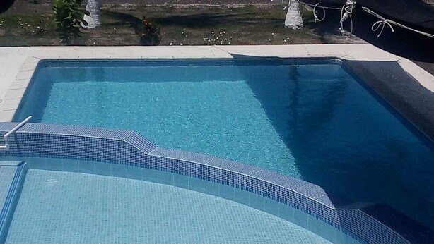 Una piscina rectangular con borde de azulejos y una sección curva.