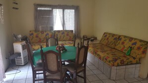 Un área de comedor con una mesa, sillas, un sofá y una ventana con cortinas.