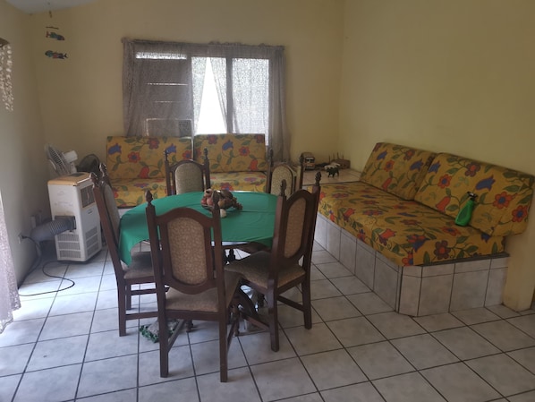 Un área de comedor con una mesa, sillas, un sofá y una ventana con cortinas.