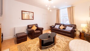 A living room with two brown leather sofas, a black coffee table, a white door, and a window with curtains. - Large and spacious 5 bedroom house in the heart of Liverpool (Fairfield)