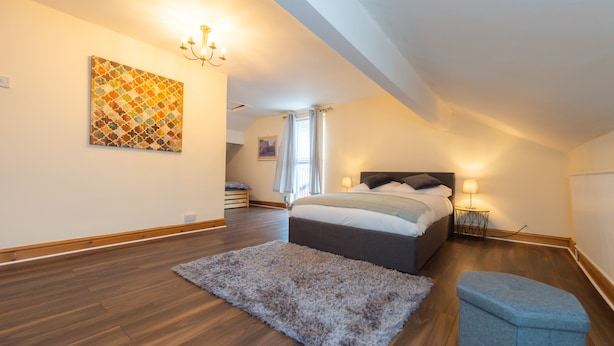 A bedroom with a large bed, a fluffy rug, a small ottoman, and a chandelier. - Large and spacious 5 bedroom house in the heart of Liverpool (Fairfield)