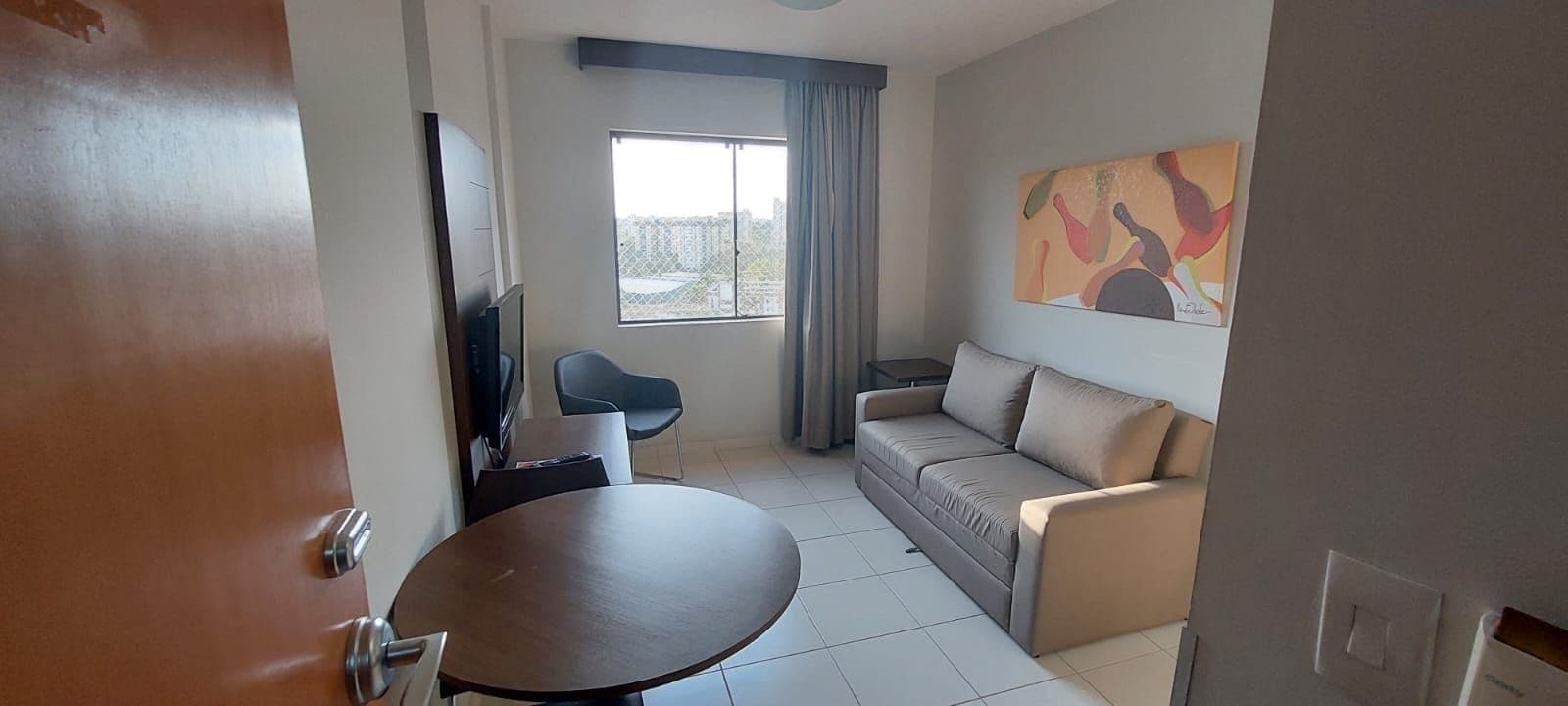 Una sala de estar con sofá, mesa, televisor y ventana con cortinas.