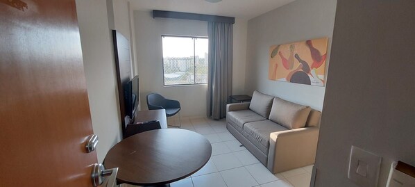 A living room with a sofa, a table, a TV, and a window with curtains. - Thermas Boulevard (Caldas Novas)