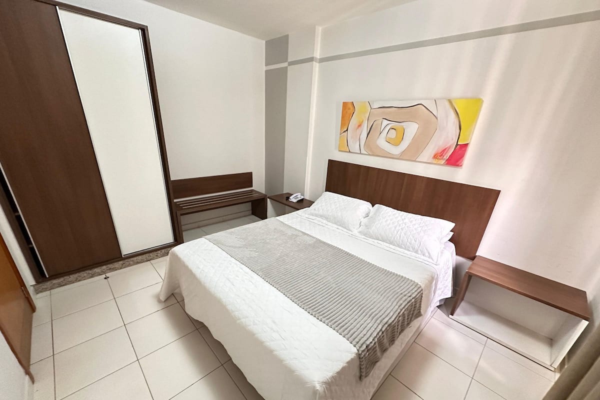 A hotel room with a bed, bedside table, and a mirror.