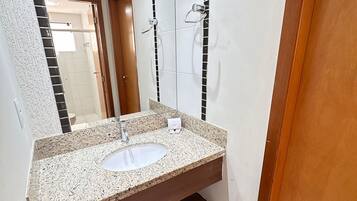 A bathroom with a granite countertop sink, a mirror, and a shower area.