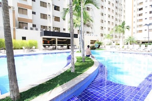 A swimming pool with lounge chairs and palm trees, surrounded by a multi-story hotel building. - Thermas Boulevard (Caldas Novas)