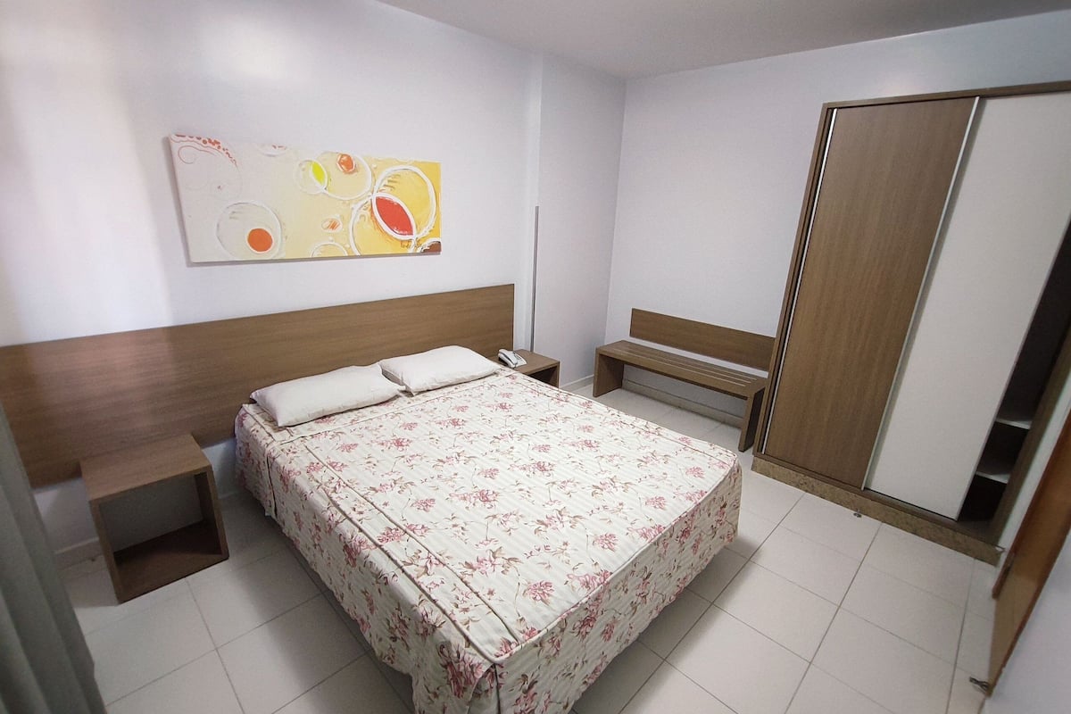 A hotel room with a bed, bedside tables, a bench, a wardrobe, and a wall art piece.