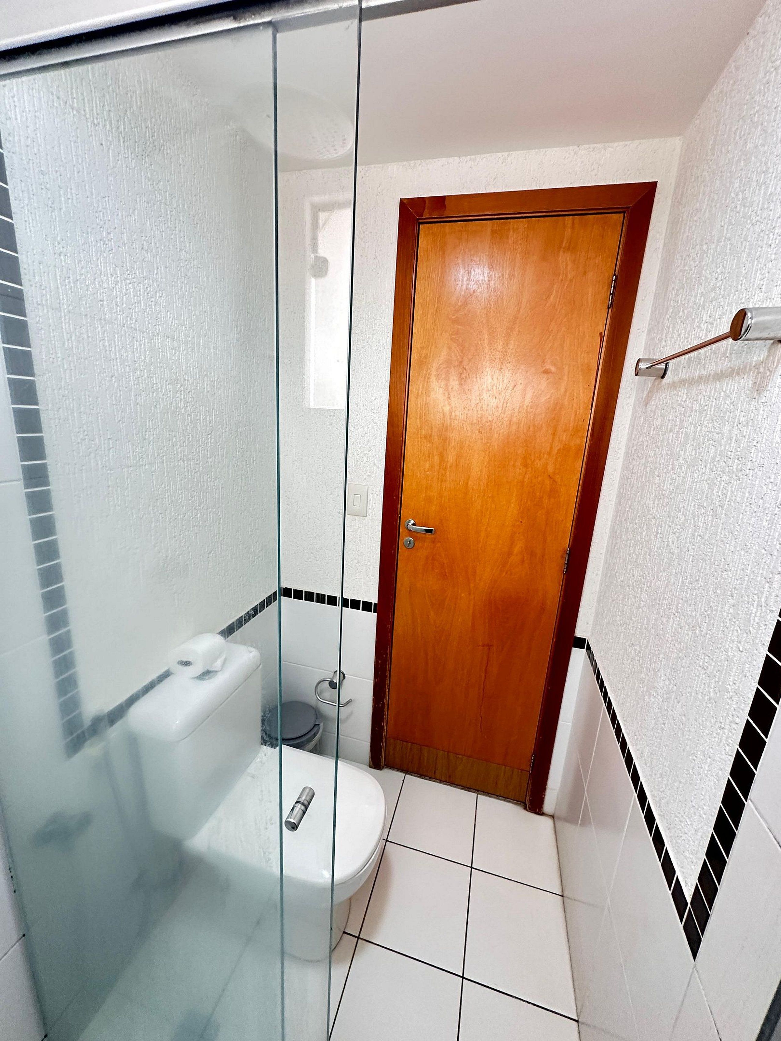 Un bagno con cabina doccia in vetro, un water e una porta in legno.