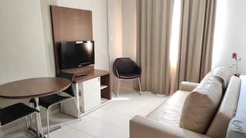 Una habitación de hotel moderna con televisor de pantalla plana, una mesa de comedor con sillas, un sofá y una ventana con cortinas.