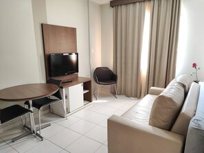 A modern hotel room with a flat-screen TV, a dining table with chairs, a sofa, and a window with curtains. - Thermas Boulevard (Caldas Novas)