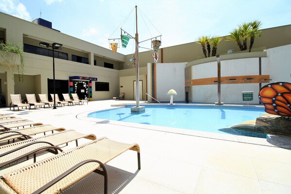 A swimming pool with lounge chairs, a basketball hoop, and a butterfly sculpture.