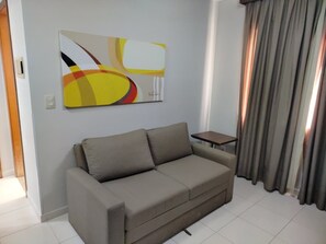 A living room with a sofa, a small table, a painting on the wall, and a window with curtains. - Thermas Boulevard (Caldas Novas)
