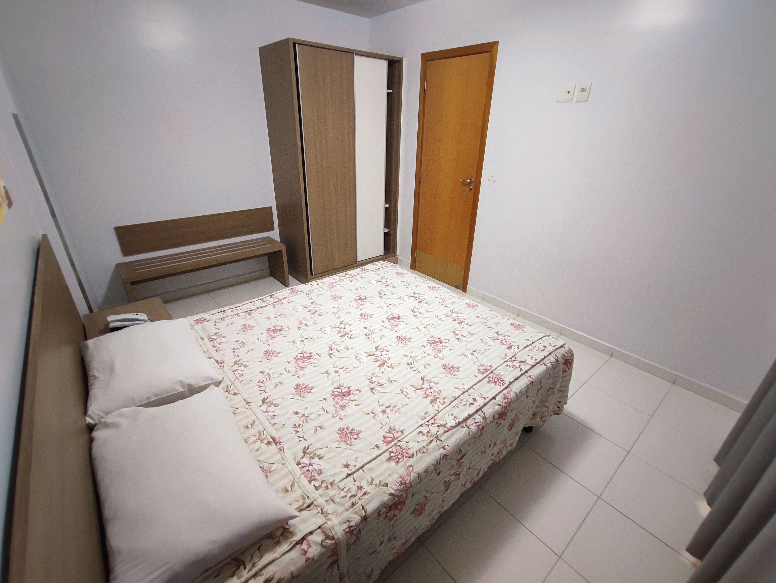 A bedroom with a bed, a wardrobe, a bench, and a door.