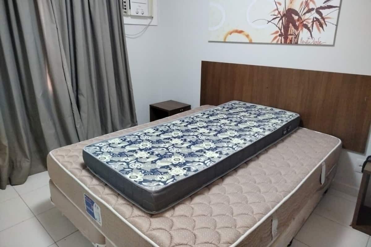 A bedroom with a bed, a headboard, a bedside table, a wall-mounted radio, and a painting.