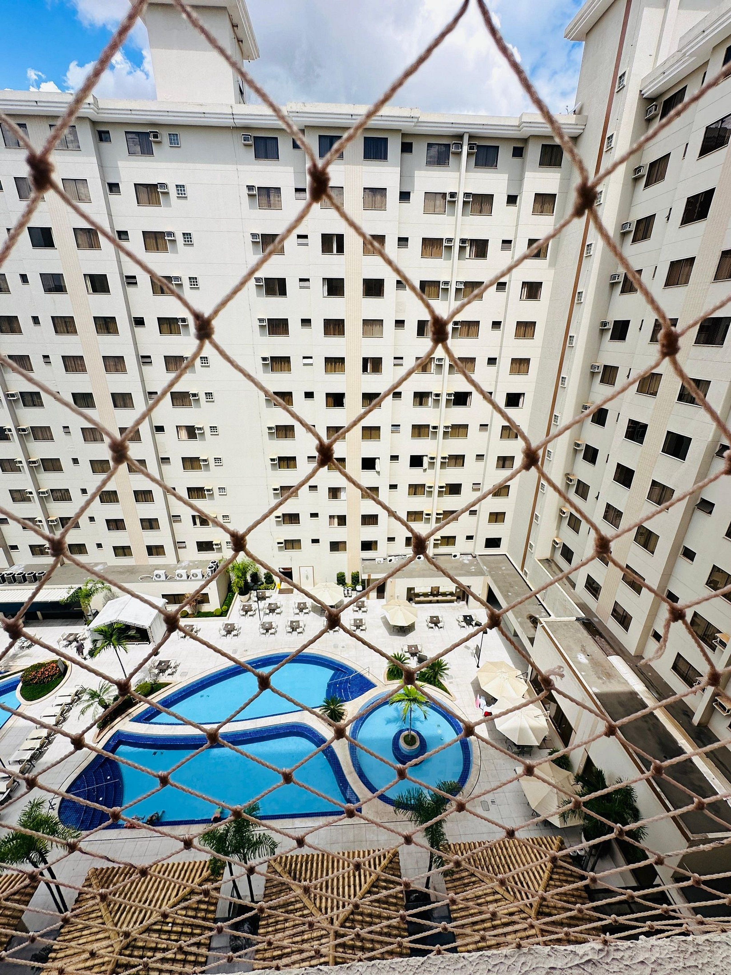 Un hotel de gran altura con múltiples pisos, un área de piscina con dos piscinas y asientos al aire libre.